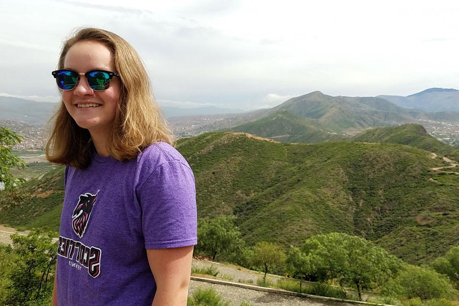 Agnes Scott study abroad student wearing sunglasses and smiling on top of a green mountain in Bolivia.